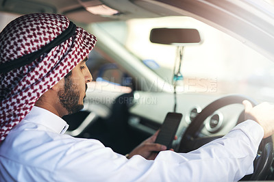 Buy stock photo Shot of a young muslim businessman using his phone while driving a car