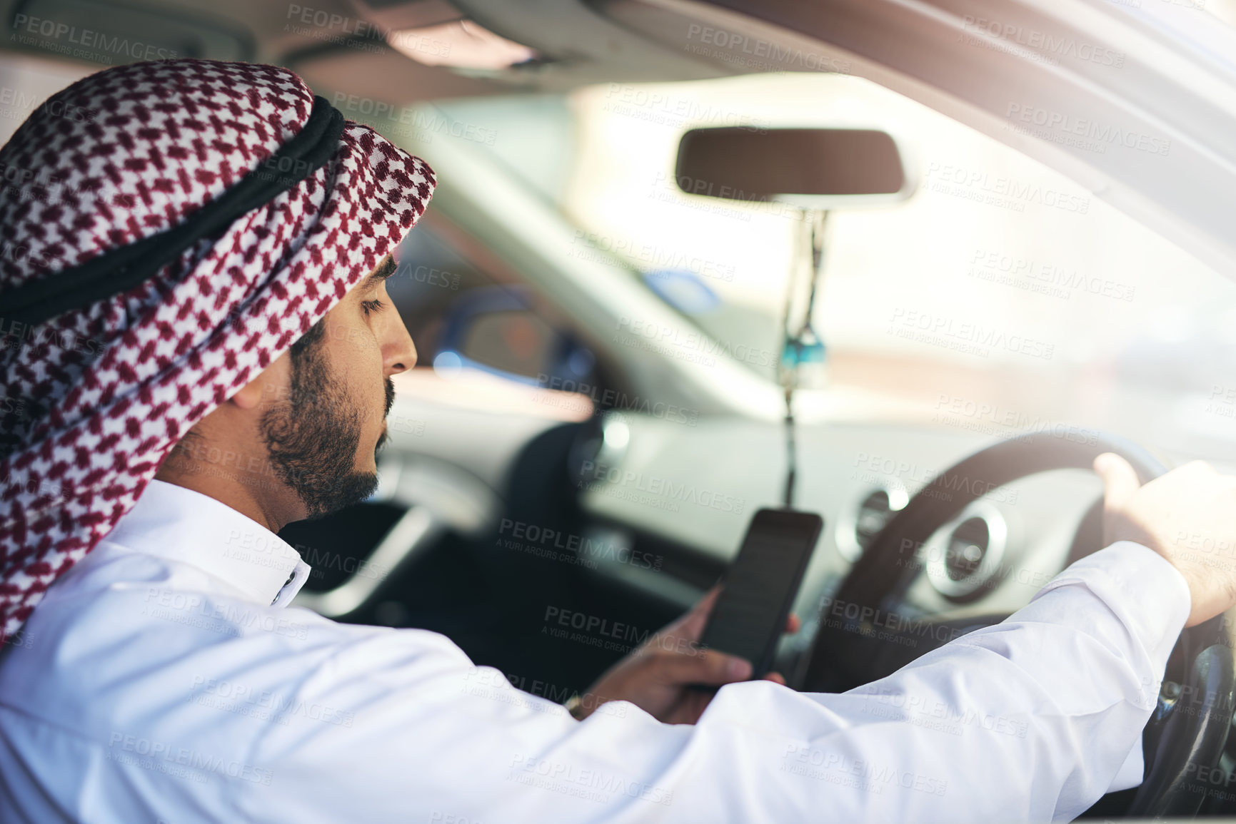 Buy stock photo Shot of a young muslim businessman using his phone while driving a car