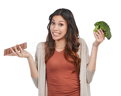 Buy stock photo Portrait of an indecisive young woman holding up a bunch of broccoli and a slab of chocolate in studio