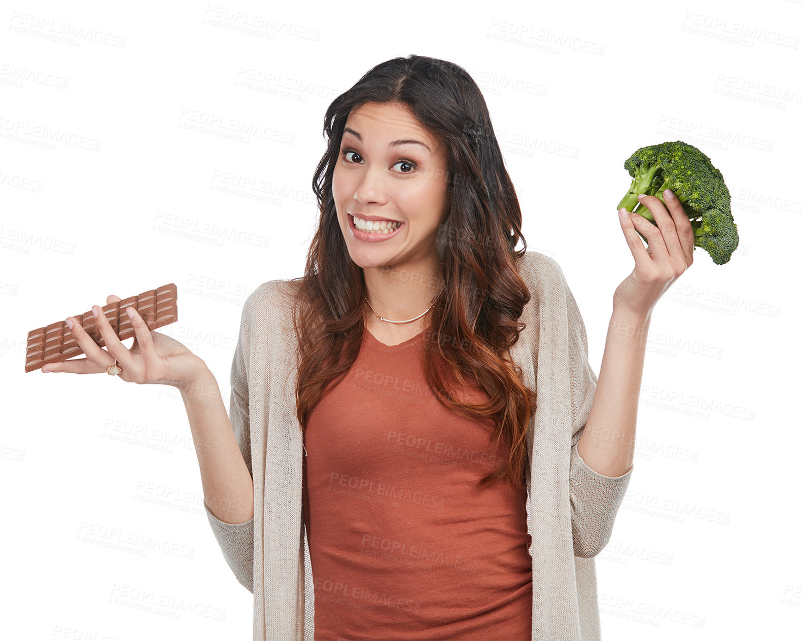 Buy stock photo Portrait of an indecisive young woman holding up a bunch of broccoli and a slab of chocolate in studio