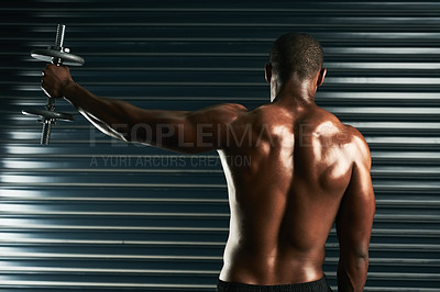 Buy stock photo Rearview shot of an athletic young man working out with a dumbbell in the studio
