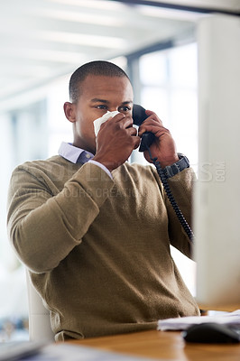 Buy stock photo Shot of a young businessman blowing his nose at his work desk
