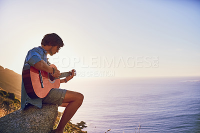 Buy stock photo Shot of a young man playing the guitar while sitting at a viewpoint outside