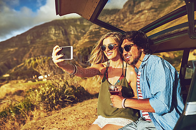 Buy stock photo Shot of a happy young couple posing for a selfie with their car on a roadtrip