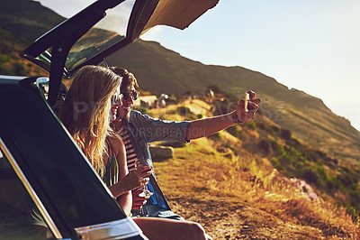 Buy stock photo Shot of a happy young couple posing for a selfie with their car on a roadtrip
