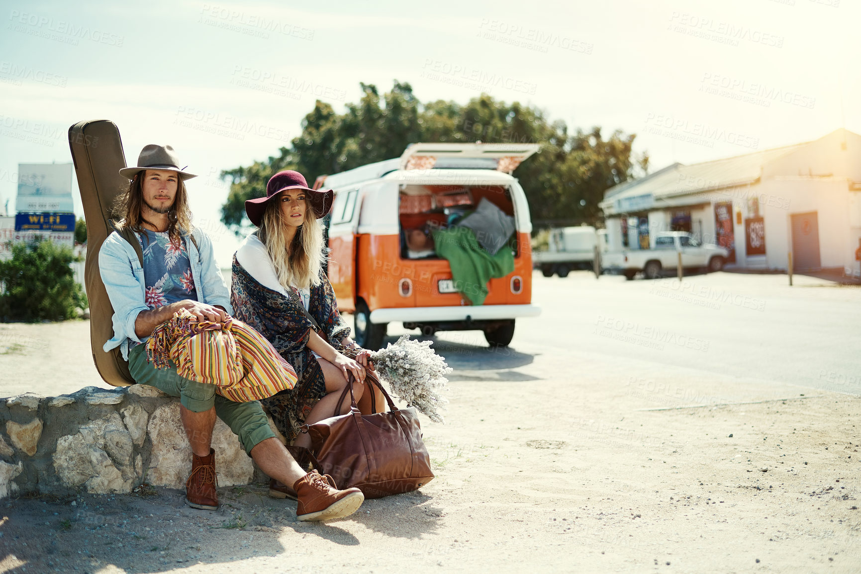 Buy stock photo Shot of a young hipster couple sitting at the side of the road with their broken down van in the background