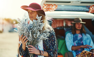 Buy stock photo Shot of a young woman standing outside with a bouquet of wildflowers with her boyfriends sitting in a van in the background