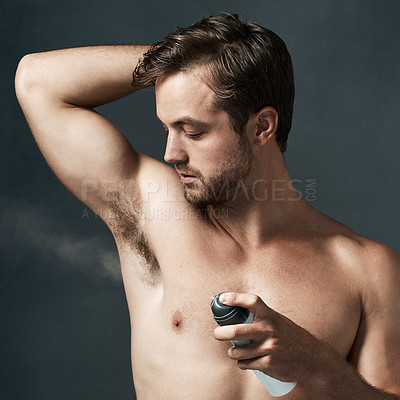 Buy stock photo Cropped shot of a handsome young man spraying deodorant on his armpit