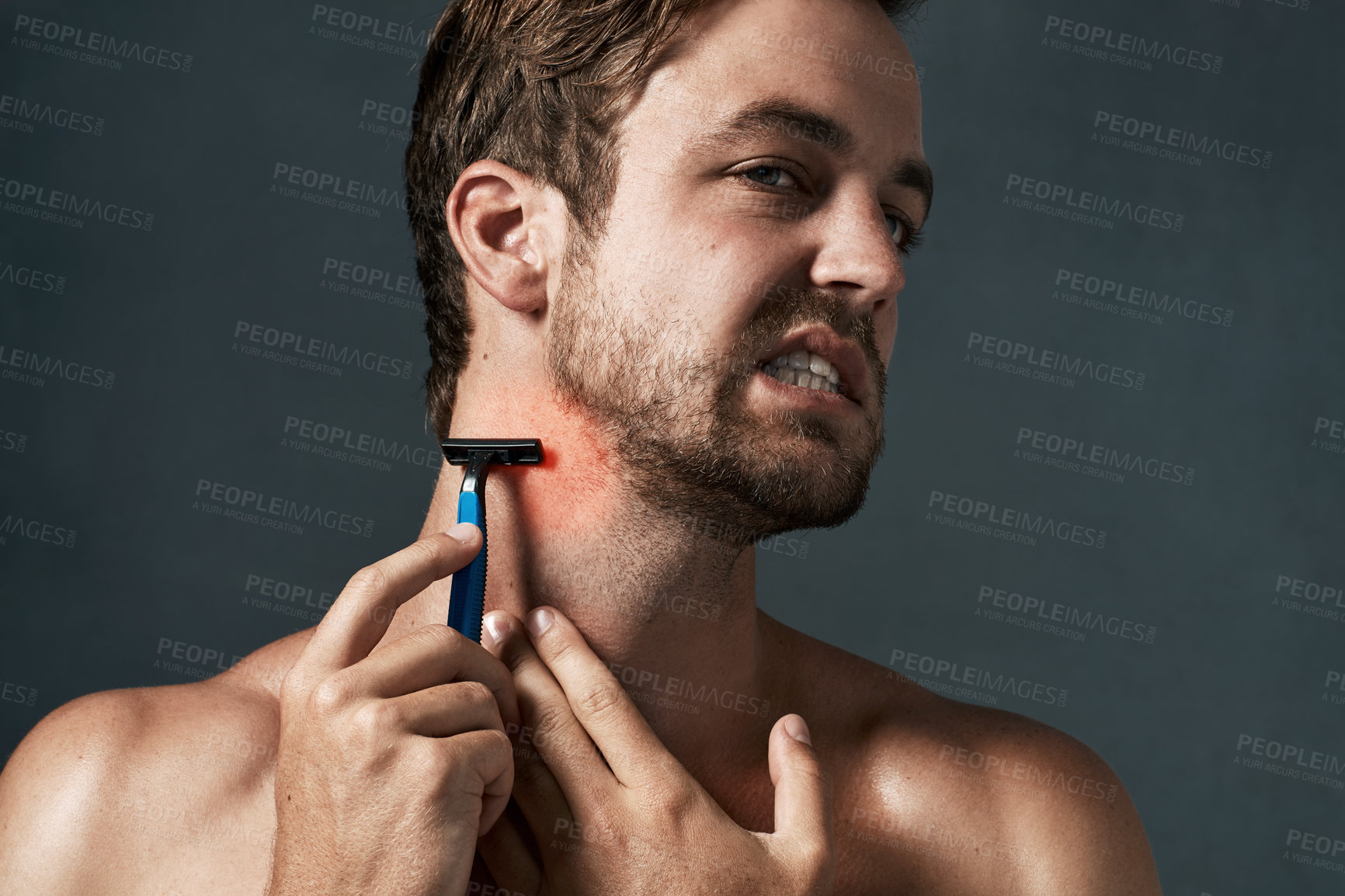 Buy stock photo Cropped shot of a handsome young man grimacing while shaving