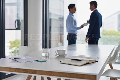 Buy stock photo Shot of paperwork on a table in an office with two businessmen having a discussion in the background