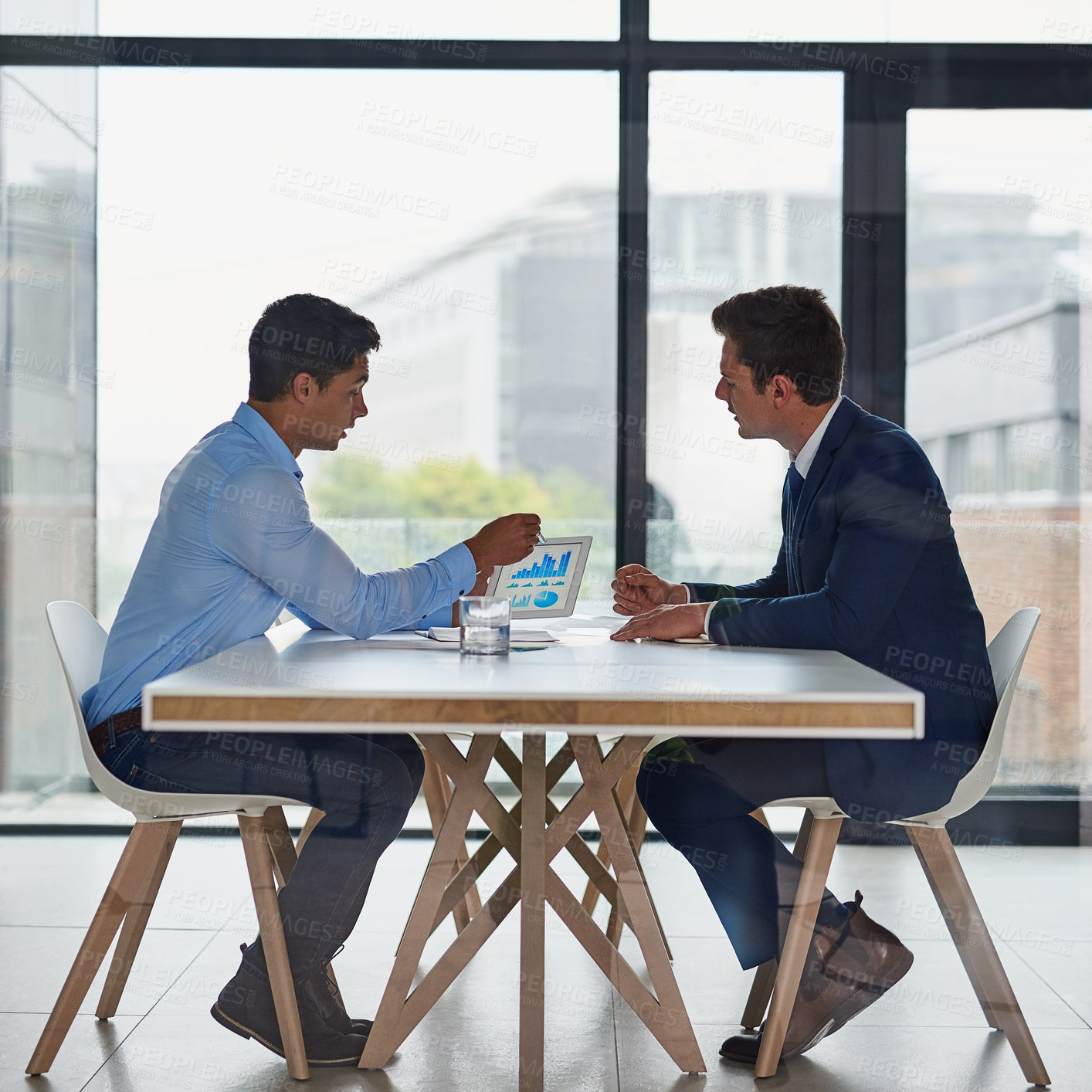 Buy stock photo Shot of two businessmen using a digital tablet during a meeting in an office