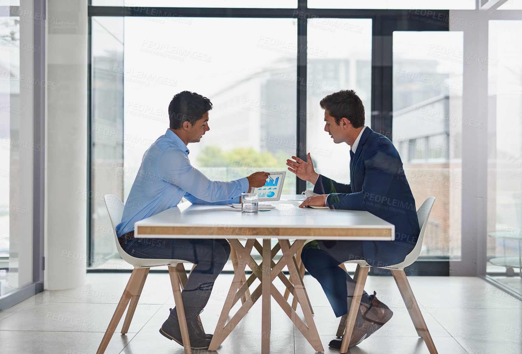 Buy stock photo Shot of two businessmen using a digital tablet during a meeting in an office