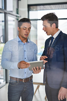 Buy stock photo Shot of two businessmen discussing something on a digital tablet in an office