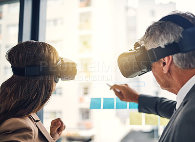 Buy stock photo Shot of two businesspeople wearing VR headsets while working with notes on a glass wall in an office