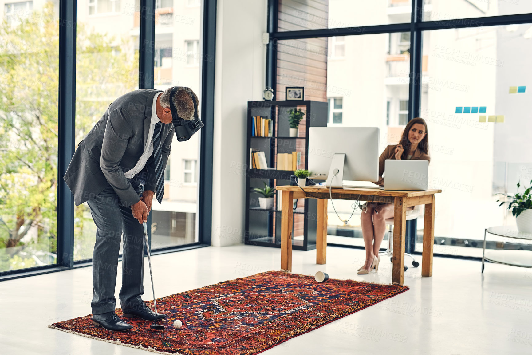 Buy stock photo Shot of a businessman wearing a VR headset while playing golf in an office