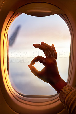 Buy stock photo Shot of a passenger making an okay sign while looking through the window of an airplane