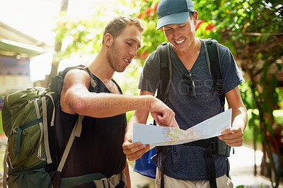 Buy stock photo Shot of two smiling young friends wearing backpacks traveling talking together over a map while in Thailand