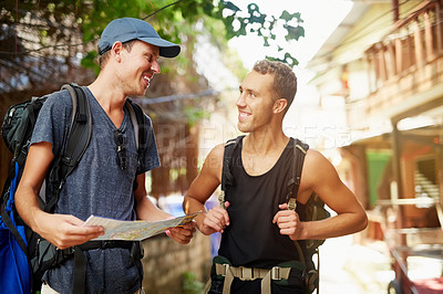 Buy stock photo Shot of two smiling young friends wearing backpacks traveling talking together over a map while in Thailand