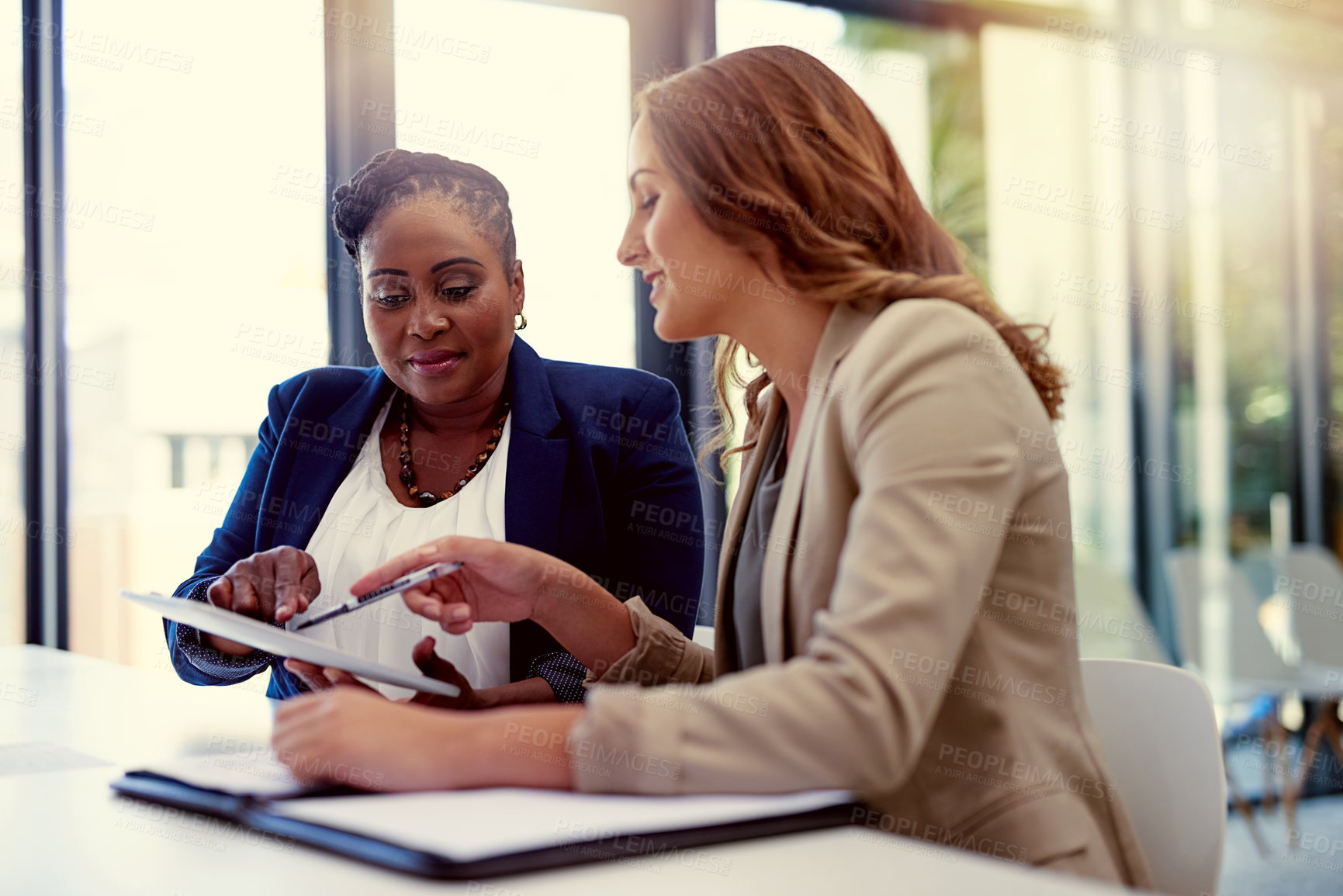 Buy stock photo Shot of two businesswomen working together on a digital tablet in an office