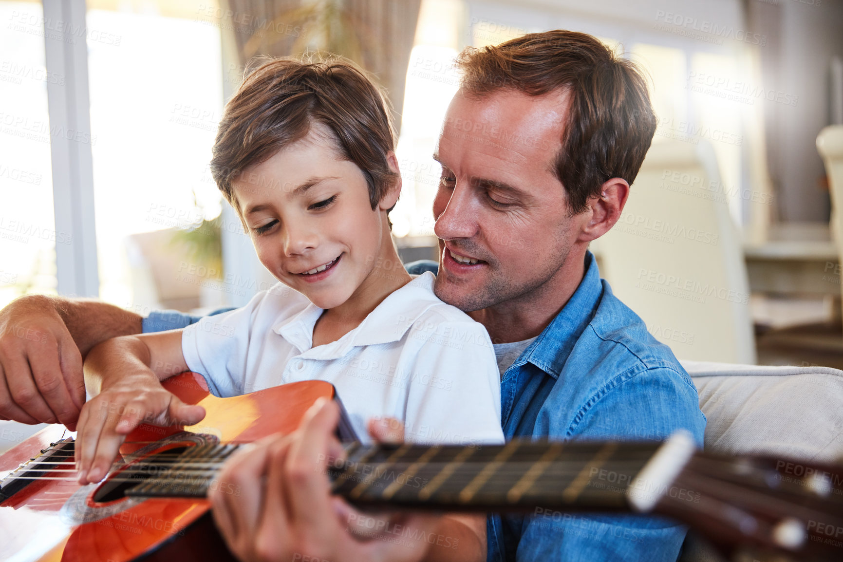 Buy stock photo Shot of a father and his young son sitting together in the living room at home playing guitar