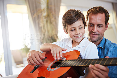 Buy stock photo Shot of a father and his young son sitting together in the living room at home playing guitar
