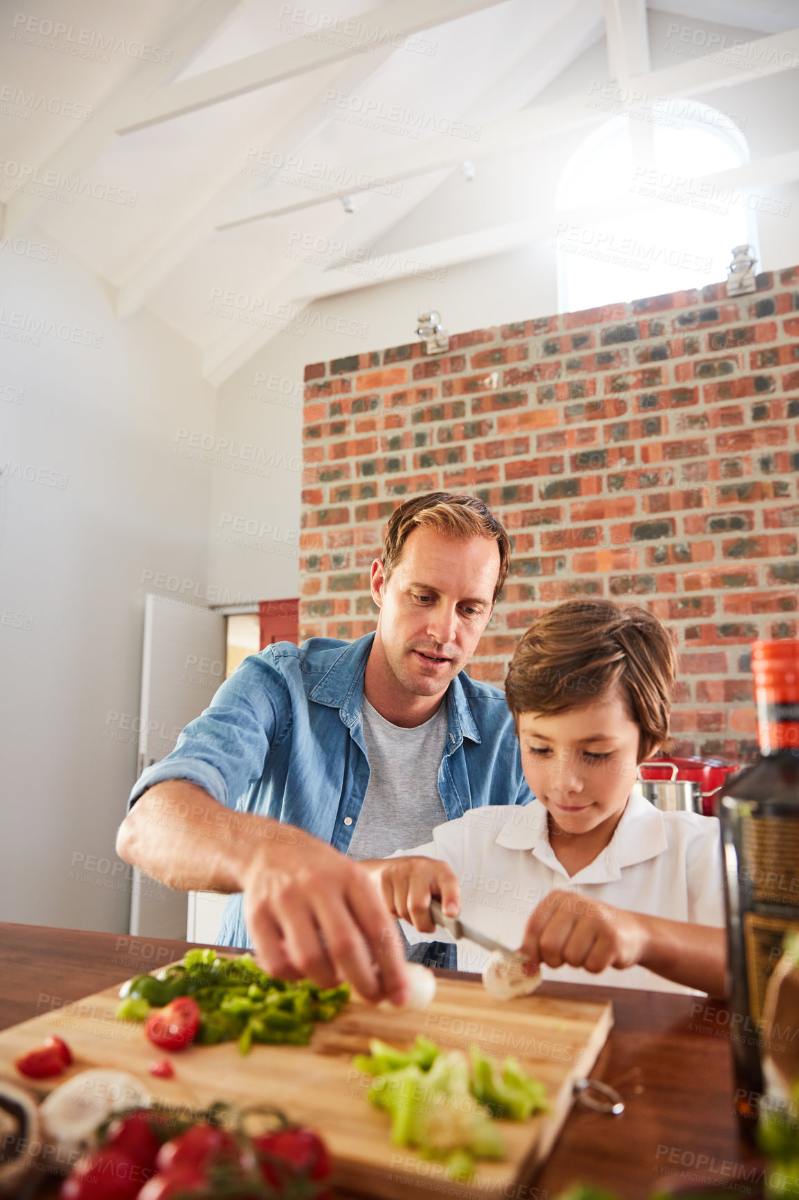 Buy stock photo Shot of a father watching his little boy chop vegetables in the kitchen