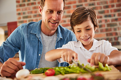 Buy stock photo Shot of a father watching his little boy chop vegetables in the kitchen