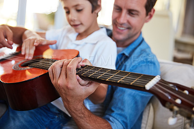 Buy stock photo Shot of a father and his young son sitting together in the living room at home playing guitar