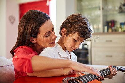 Buy stock photo Shot of a mother and her young son sitting together in the living room at home playing guitar