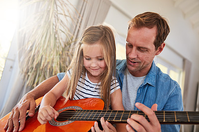 Buy stock photo Shot of a father and his young daughter sitting together in the living room at home playing guitar