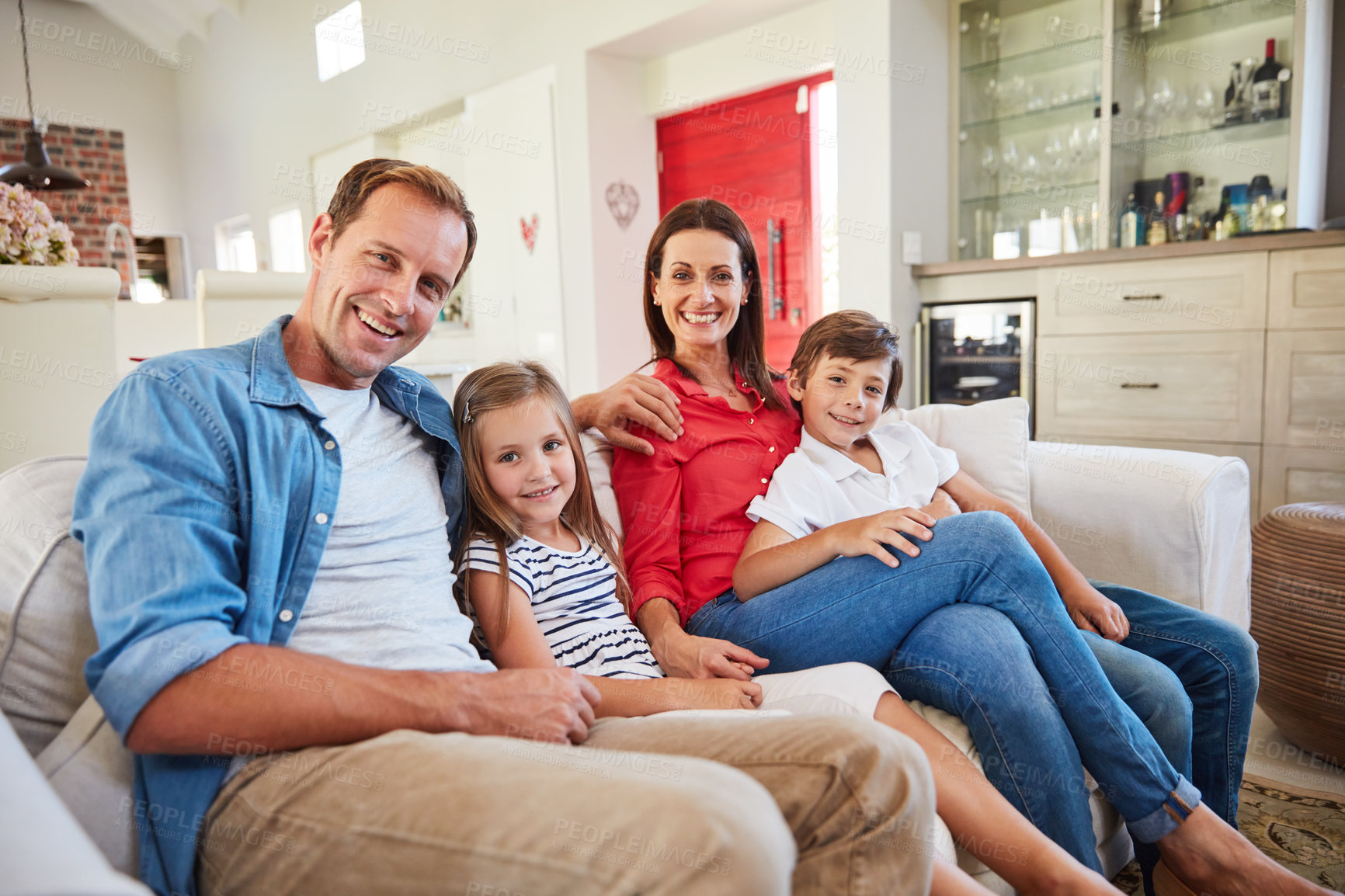 Buy stock photo Portrait of smiling parents sitting with their young son and daughter on their living room sofa at home