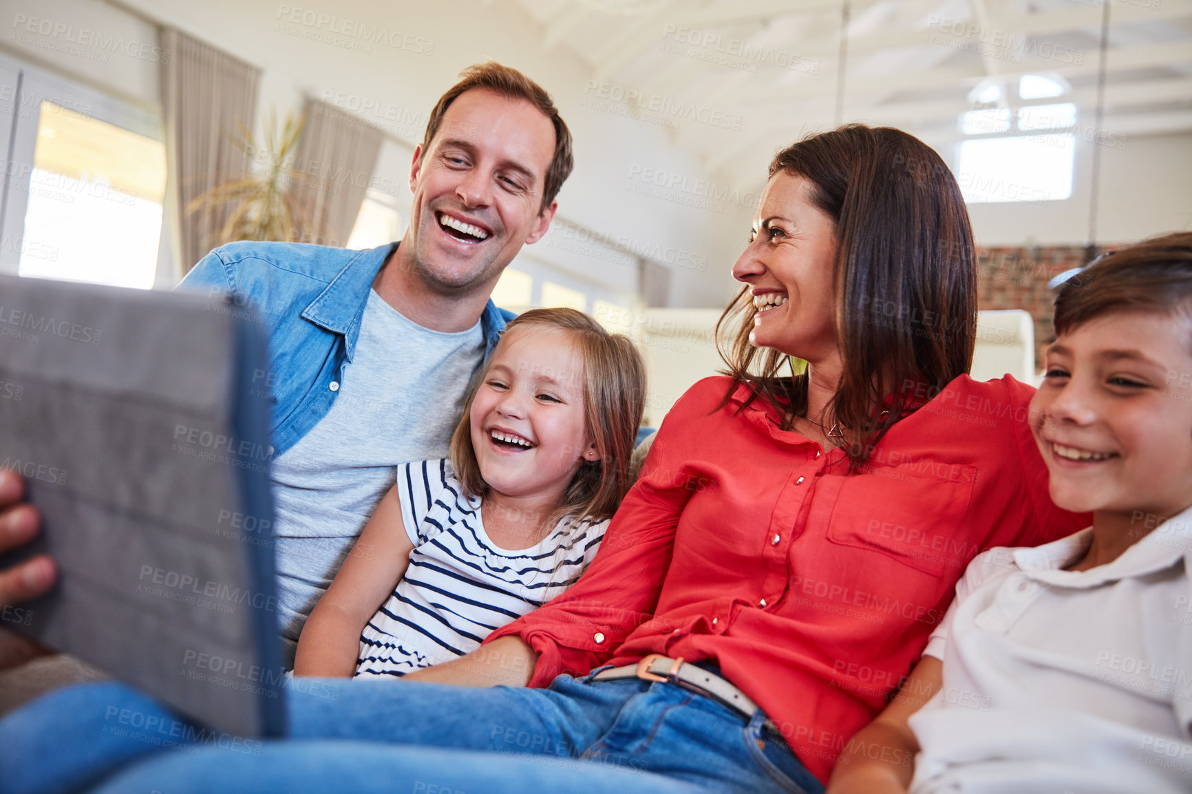 Buy stock photo Shot of smiling parents sitting with their young son and daughter on their living room sofa at home using a digital tablet