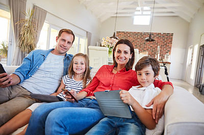 Buy stock photo Portrait of a smiling family sitting together on their living room sofa using various media and devices