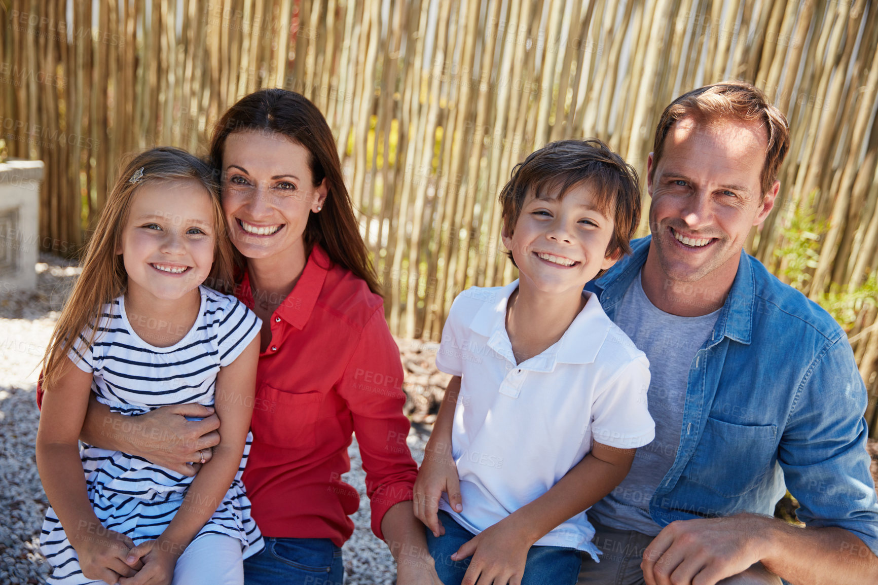 Buy stock photo Portrait of smiling parents and their young son and daughter sitting outside in their yard on a sunny day