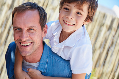 Buy stock photo Portrait of smiling father giving his young son a piggyback outside in their yard on a sunny day