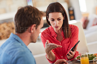 Buy stock photo Shot of an angry woman confronting her husband over something on his phone during lunch
