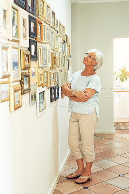Buy stock photo Shot of a happy senior woman admiring a collection of framed photographs in her home