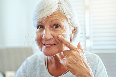 Buy stock photo Portrait of a happy senior woman applying skin cream to her face at home