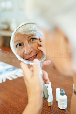 Buy stock photo Shot of a senior woman using a hand mirror to look at her skin at home
