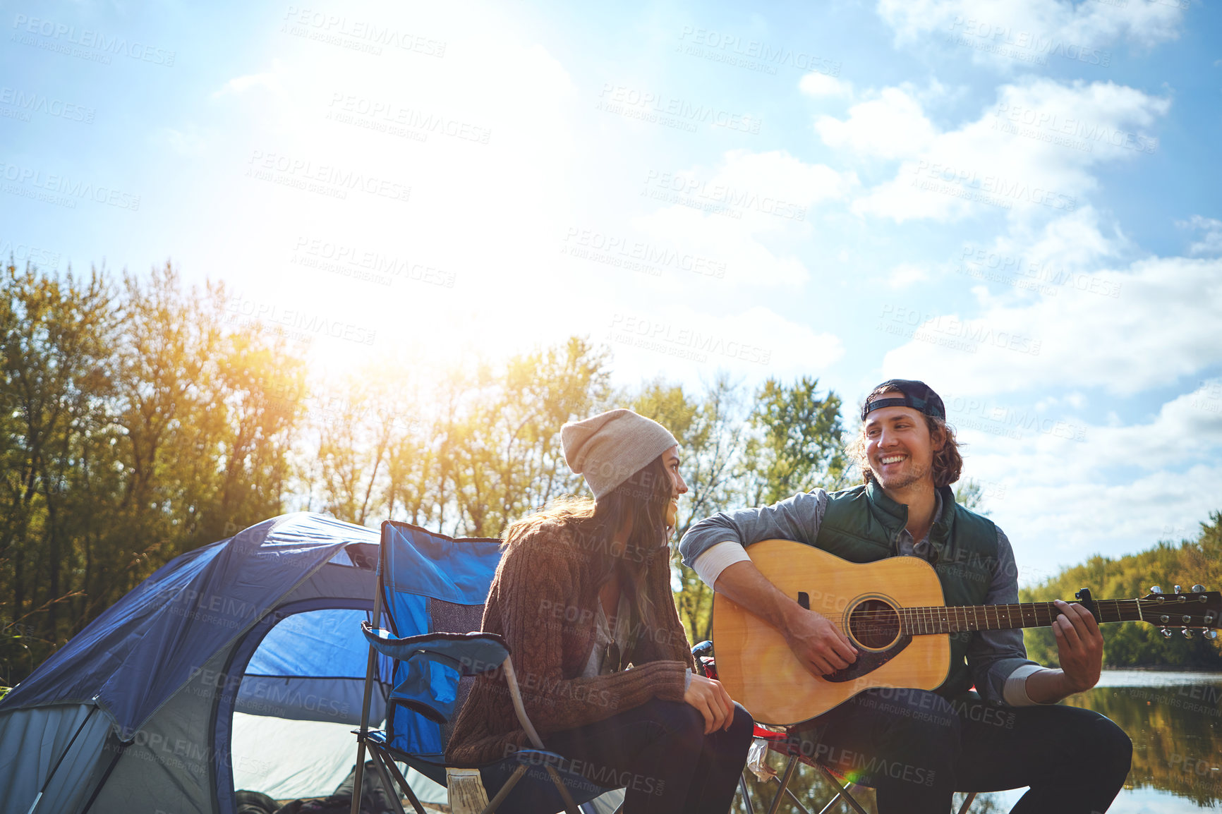 Buy stock photo Shot of a young man playing his girlfriend a song on his guitar while out camping