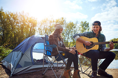 Buy stock photo Shot of a young man playing his girlfriend a song on his guitar while out camping