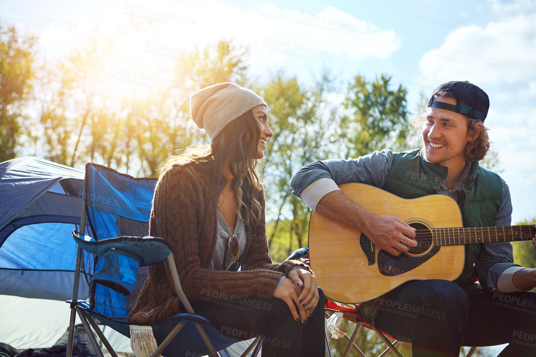 Buy stock photo Shot of a young man playing his girlfriend a song on his guitar while out camping