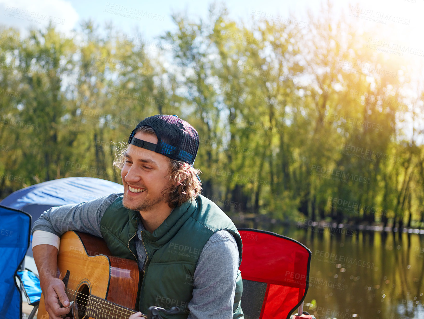 Buy stock photo Shot of a young man playing his guitar while out camping