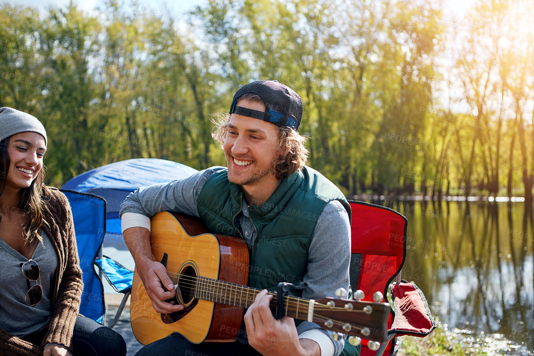 Buy stock photo Shot of a young man playing his girlfriend a song on his guitar while out camping