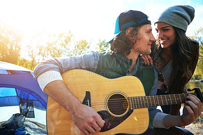 Buy stock photo Shot of a young man playing his girlfriend a song on his guitar while out camping