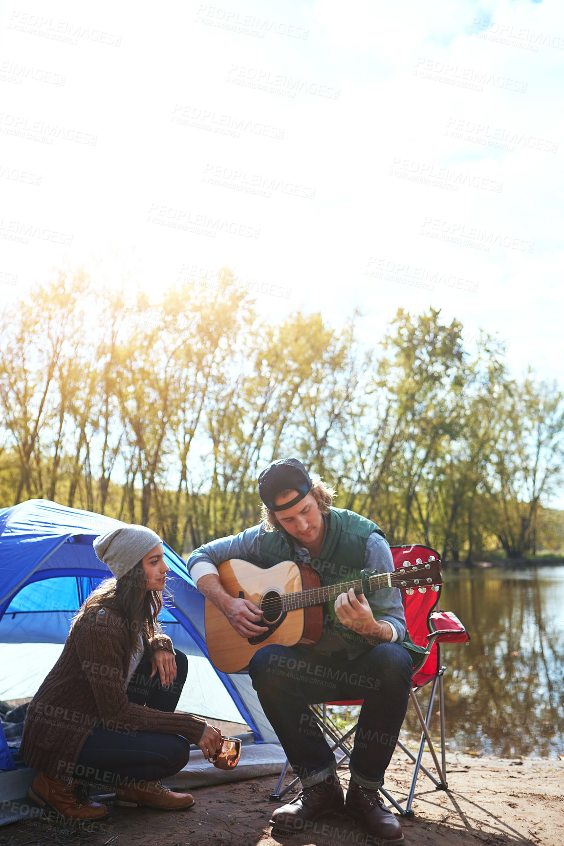 Buy stock photo Shot of a young man playing his girlfriend a song on his guitar while out camping