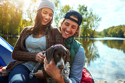 Buy stock photo Couple, dog and with love for camping in forest, sunshine and bond for smile by support of animal on adventure time. Happy, woman and man with puppy pet for care, hug or relax in summer journey