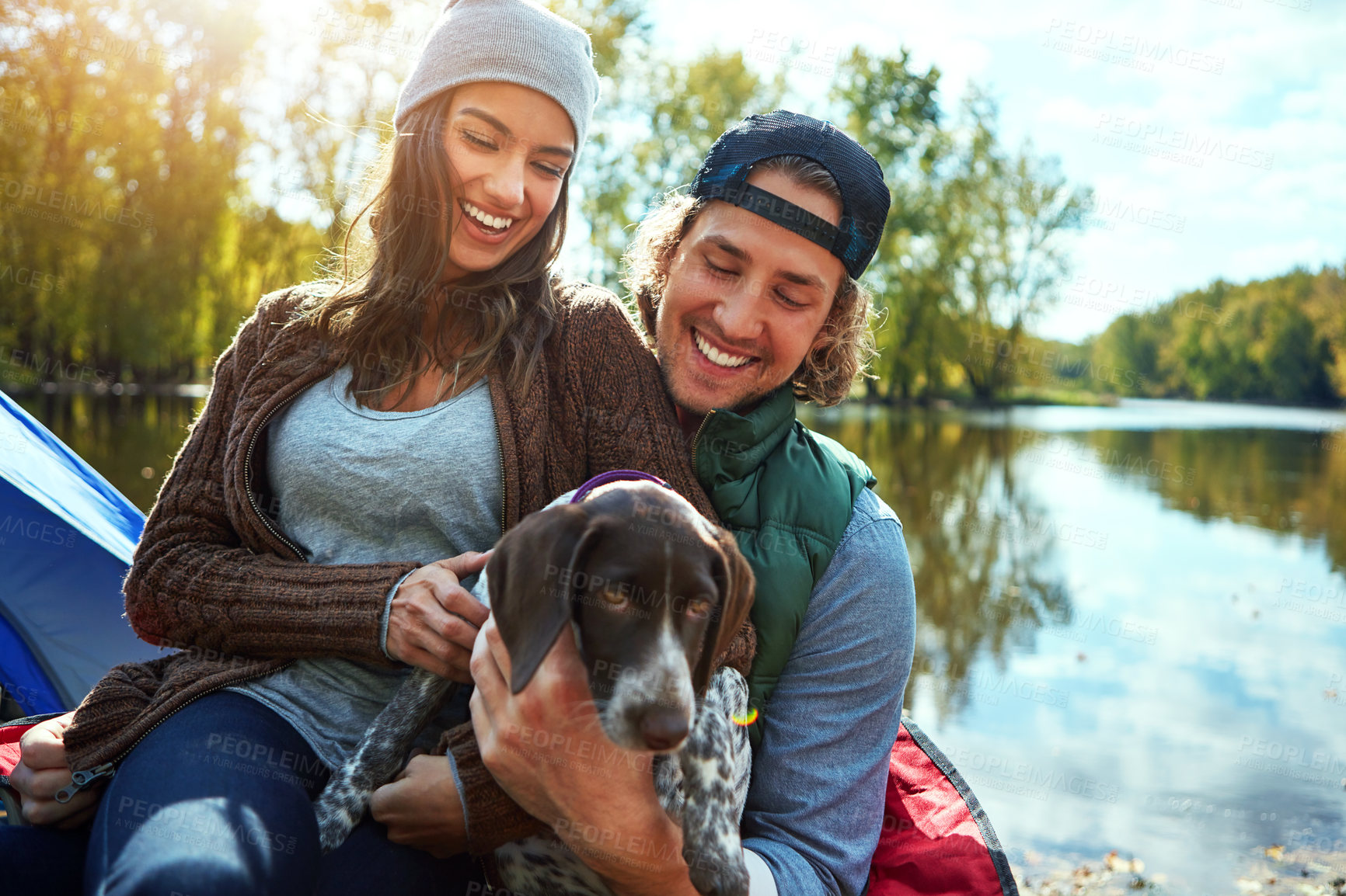 Buy stock photo Couple, dog and with love for camping in forest, sunshine and bond for smile by support of animal on adventure time. Happy, woman and man with puppy pet for care, hug or relax in summer journey