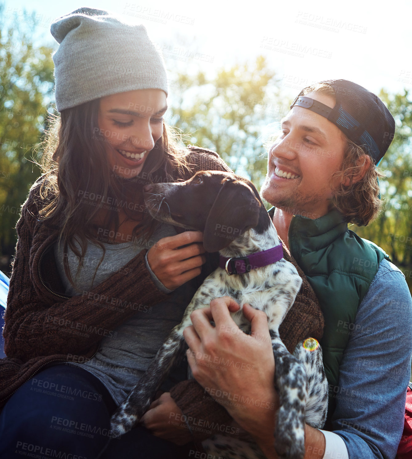 Buy stock photo Camping, couple and dog with love in nature forest, sunshine and bonding, smile and support of animal on adventure time. Happy, woman and man with puppy pet for care, hug or relax in summer journey