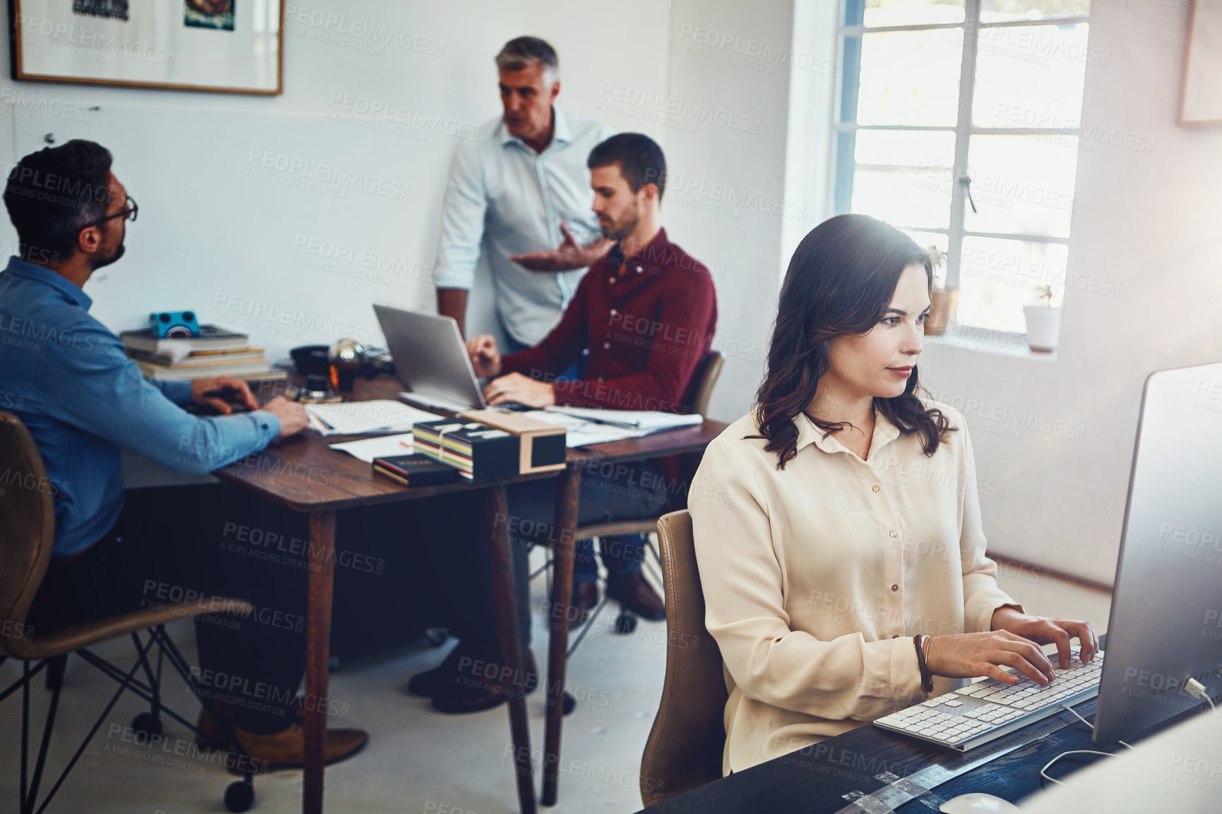 Buy stock photo Shot of a young woman working in the office with her colleagues in the background